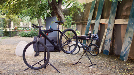 Black modern bicycles await fine-tuning and adjustment with expert equipment in backyard as summer hobby. Outside broken bike is placed on repair-stand for meticulous examining and correcting.の写真素材