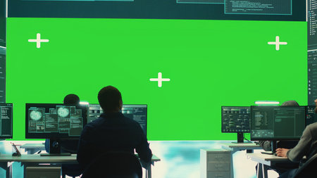 Team of hackers look at green screen in high tech agency office, working together on hacking database systems for cyberwarfare activity. Experts conducting scams. Camera A.の写真素材