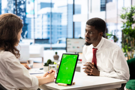 Job interview candidate interested in career advancement, talking with HR employee using green screen tablet. Man talking with recruiter checking his CV on chroma key device to get hiredの写真素材