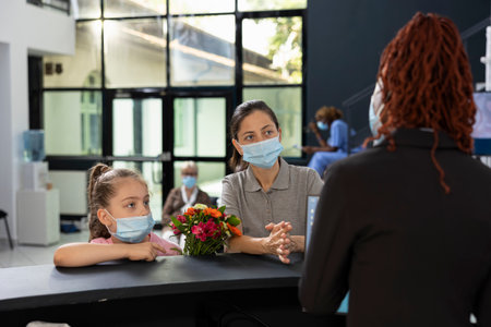Child and mother respecting hospital safety rules at the reception for patient visit, filling in registration forms with the receptionist to be on the visitors list at hospital. Modern clinic.の写真素材