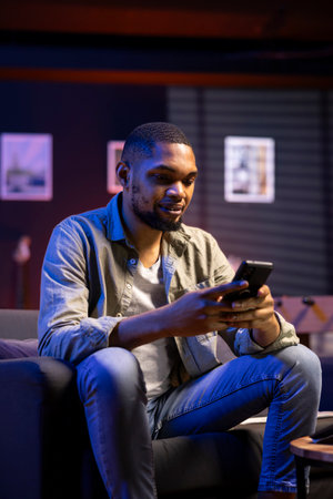 Chill self employed guy enjoying a break with his mobile phone on sofa, texting friends on social...
