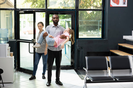Girl fainted and her african american father is carrying her in the hospital, waiting for immediate...