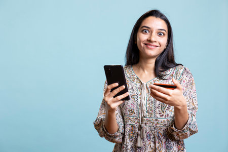 Smiling female buyer excited to purchase stuff online on websites in the studio, adding payment...