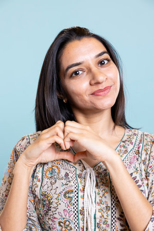 Portrait of sweet loving woman shows heart shaped symbol with hands, showing kindness and gratitude. Happy affectionate girlfriend doing tender love symbol for boyfriend in the studio.の写真素材