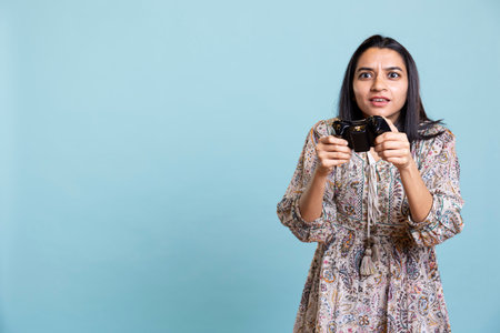 Confident thrilled gamer smiling and paying attention on the video competition, e sport tournament on her mobile phone. Young indian woman enjoying interactive gameplay in studio.の写真素材