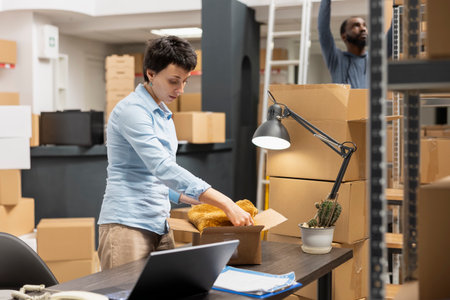 Woman depot employee handling custom orders and packages, working in a supply room surrounded by shelves filled with products. Small scale local shipping operations, delivery logistics.の写真素材