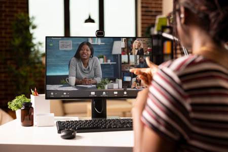 Back view of businesswoman in home workspace, discussing project plans with teammates in video conference. Multiethnic team members join online meeting, working remotely from individual locations.の写真素材