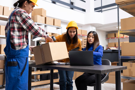 Group of asian workers managing business logistics in a retail warehouse, applying shipping labels, preparing invoices and organizing shelves for small scale delivery and fulfillment.の写真素材