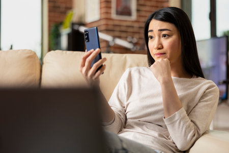 Self employed financial advisor sitting on couch in living room, listening to client during online meeting. Confident businesswoman with cellphone, reviewing marketing strategy with colleague remotelyの写真素材