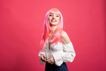 Attractive caucasian woman with pink hair joyfully posing against isolated background. Beautiful female individual with hands together, striking a cute model stance with cheerful expression.の写真素材