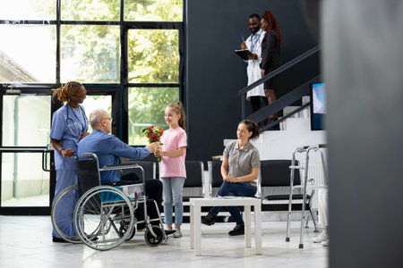 Young child offering flowers to grandfather wheelchair user during patient visit, showing intergenerational love and support under hospital safety rules. Kid supporting grandparent.の写真素材