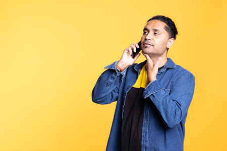 Indian person smiling during a conversation with his group of friends, chatting on telephone line against an orange background. Young adult with a man bun in casual attire gossiping.の写真素材