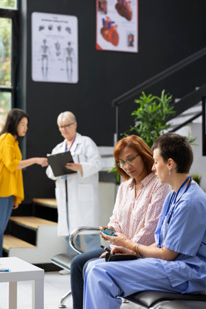 Nurse assisting asian patient in measuring her sugar levels with glucometer for a routine checkup in waiting room. Specialist explains diabetes reading interpretation for glucose levels.の写真素材