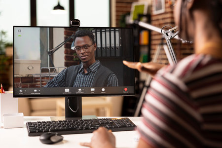 Male business advisor seen on computer screen, providing insights on strategy plans to black female entrepreneur during video call. African american individuals having virtual meeting on desktop pc.の写真素材