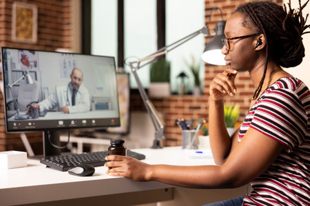 Self employed woman speaking with doctor on video call, discussing diagnosis and side effects while holding prescription medication. Remote female patient consults physician from home.の写真素材