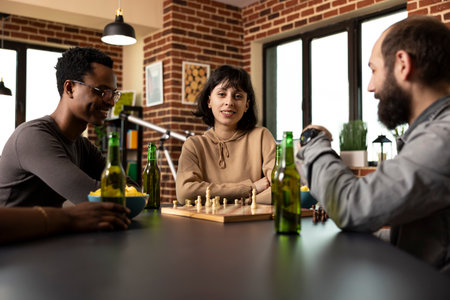 Caucasian woman with arms crossed, sitting in the middle of male friends during chess match in brick wall room. Selective focus on young lady looking at camera as others enjoy board game session.の写真素材
