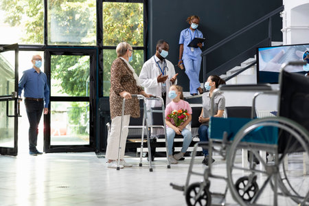 Child gives flowers to grandmother with walking frame during clinic visit, showing family love and support while following safety rules, healthcare protection. Different generations at facility.の写真素材