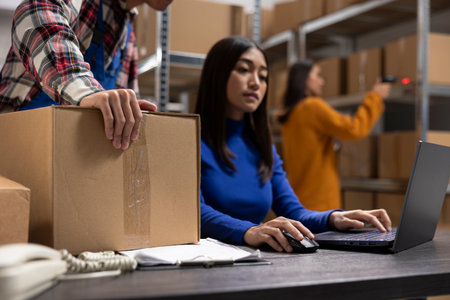 Asian depot team packing boxes at packaging station for small business, managing orders for the local brand in warehouse. Employees prepare merchandise for growing distribution hub.の写真素材