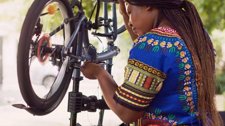 African american female cyclist doing maintenance on damaged bike tire rubber with specialized multitool. Up-close view of black woman grabbing screwdriver for tightening bicycle parts.の写真素材