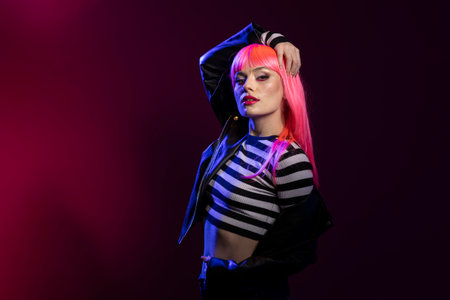Fierce female individual displays sharp gaze and expressive makeup beneath glowing studio lights. Young woman model stands poised in fashionable outfit posing confidently during photo session.の写真素材
