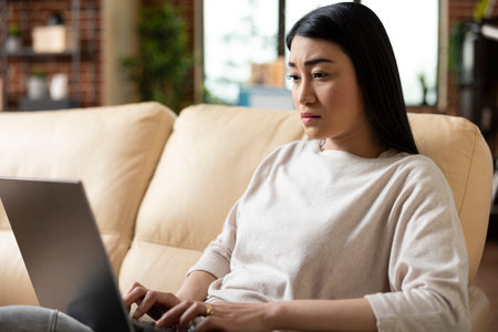 Focused female entrepreneur typing on laptop, managing business analytics and replying to professional emails. Confident businesswoman balancing tasks efficiently in relaxed living room.の写真素材