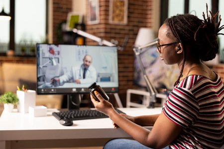 African american woman seated at desk talking to caucasian doctor on video call. Black female entrepreneur holds pill bottle, discussing prescription and treatment during online medical consultation.の写真素材