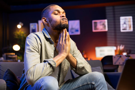 Concerned african american man struggling with task deadlines and work pressure, being stressed and worried about his future. Frustrated scared person working remotely on the couch.の写真素材