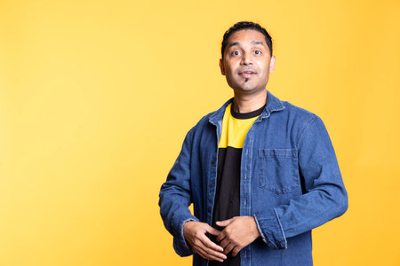 Portrait of cheerful confident indian man smiling standing against orange background, looking pleased in the studio. Happy expressive person in traditional attire grinning, feeling satisfiedの写真素材