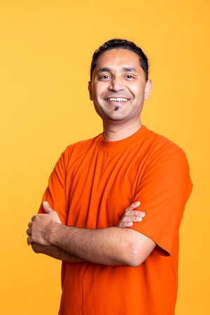 Portrait of jolly indian man smiling and posing with arms crossed standing against studio background. Joyous upbeat male person in casual clothing showcases positive emotions.の写真素材