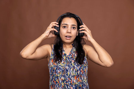 Portrait of female model wearing headphones, reacting to surprising audio content with an expressive face. Astonished woman with wide eyes and open mouth stares at camera, stunned by what she hears.の写真素材
