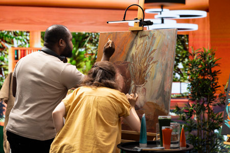 Team of skilled artist collaborating on a rustic painting in art studio, using creative painting techniques with brushes and watercolor paint. Applying multicolored dye with careful brushstrokes.の写真素材