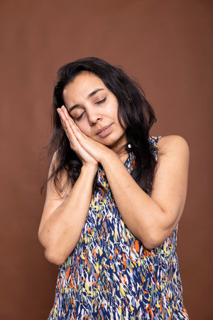 Exhausted woman with her head on hands, appearing sleepy and in need of rest. Female adult posing as if dreaming or napping while standing, expressing peace and tiredness against isolated background.の写真素材