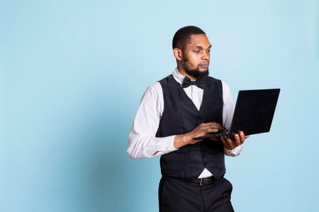 Bellhop employee making online remote reservations on laptop, browsing the hotel website to check lodging and availability. Doorkeeper staff gives assistance to guests.の写真素材