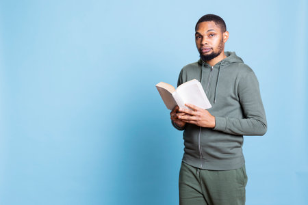 Confident happy person reading a book against blue background, feeling pleased and enjoying his...