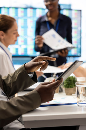 Shareholder examining infographics and resource allocation on tablet, gathering with associates for a strategy session. Utilizing data analytics to develop innovative solutions for growth.の写真素材