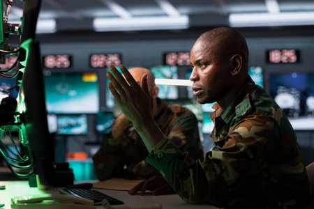 Military officer looking at surveillance monitor, analyzing data to allocate resources to units based on mission needs. African american agent examining strategic data on screenの写真素材