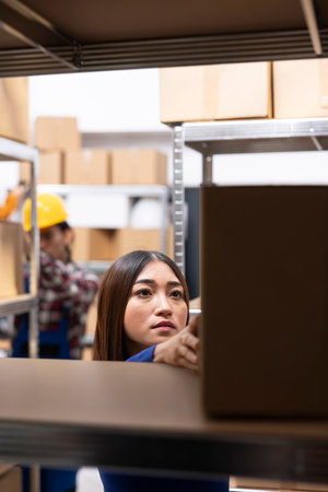 Asian female staff at a small business supply room handles merchandise and prepares shipments, ensuring local delivery. Local brand operations include express delivery, inventory tracking.の写真素材