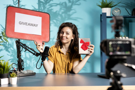 Social media influencer announcing giveaway for audience with cardboard sign, holding gift box, explaining how to win prize. Woman using copy space board to instruct her online community about contestの写真素材