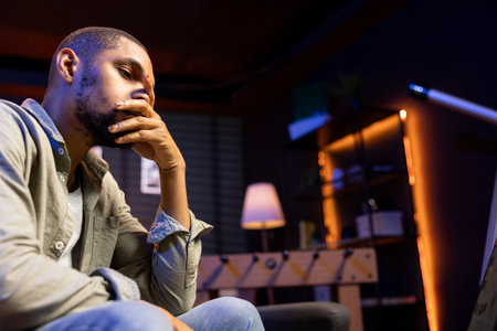 African american person receiving some bad news while doing remote work tasks, feeling overworked and under pressure to complete all his assignments. Young adult deals with burnout.の写真素材