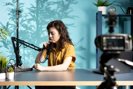 Content creator positioning professional microphone closer, ensuring it captures clear audio for upcoming video. Vlogger checks audio levels, making slight adjustments to balance soundの写真素材