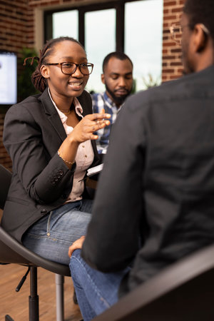Female business consultant with glasses provides financial advice to black man in brick wall office. African american woman manager discusses a company project while questioning her male employee.の写真素材