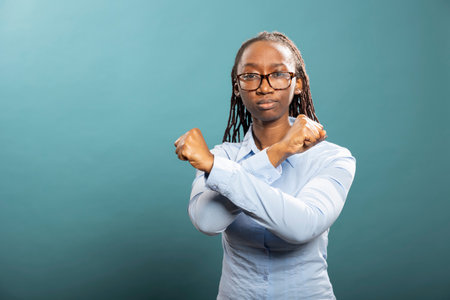 Confident african american woman poses in studio with her arms crossed in an X gesture. Black female individual looks directly at camera, expressing strength, rejection and bold determination.の写真素材