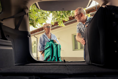 Senior couple loading their luggage in the car trunk for a vacation drive and preparing with road essentials. Retired excited people embrace the free time and comfort of travelling together.の写真素材