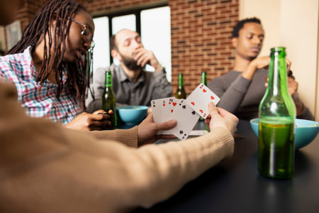 White woman holds playing cards, considering next move during friendly match with friends at home. Selective focus shows lady in action, chilling with diverse group, hanging out in cozy room.の写真素材