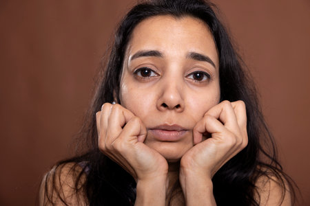 Closeup of sad indian woman looking directly at camera with troubled, distressed expression. Anxious female model resting head on her hands, feeling emotional after receiving upsetting newsの写真素材