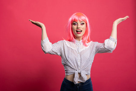Female model with cheerful expression and open gesture presents space designed for advertisement. Joyful woman stretches arms wide, smiling brightly and standing against isolated background.の写真素材