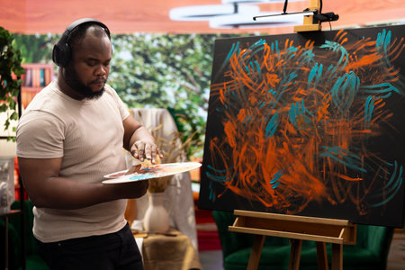 Artist listening to music and creating an abstract painting with his fingers, showing his skills and contemporary ideas in art studio. Creative process finger painting for vibrant artwork.の写真素材