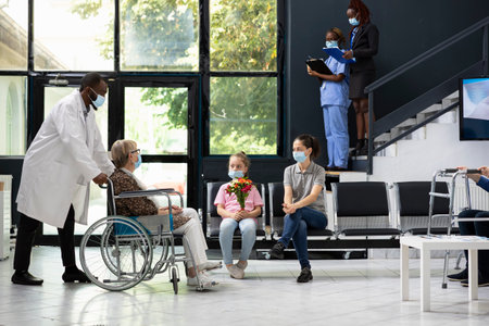 Little girl offering flowers during visiting hours with grandma in wheelchair, offer bouquet and respecting hospital safety or hygiene standards. Medical regulations to visit patients at hospital.の写真素材
