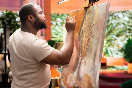 African american artist using his skill to paint a new creation in art studio, using innovative painting technique for his masterpiece. Young contemporary painter working on an artwork.の写真素材