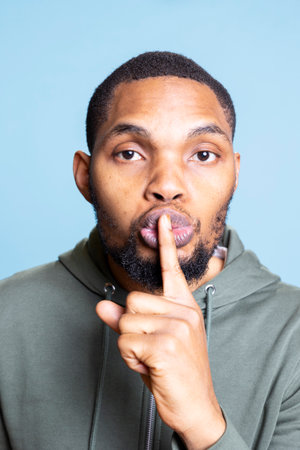 Private african american adult covering his lips and doing a hush sign to be quiet, keeping a secret with confidential information. Young person showing the mute symbol in order for peace.の写真素材